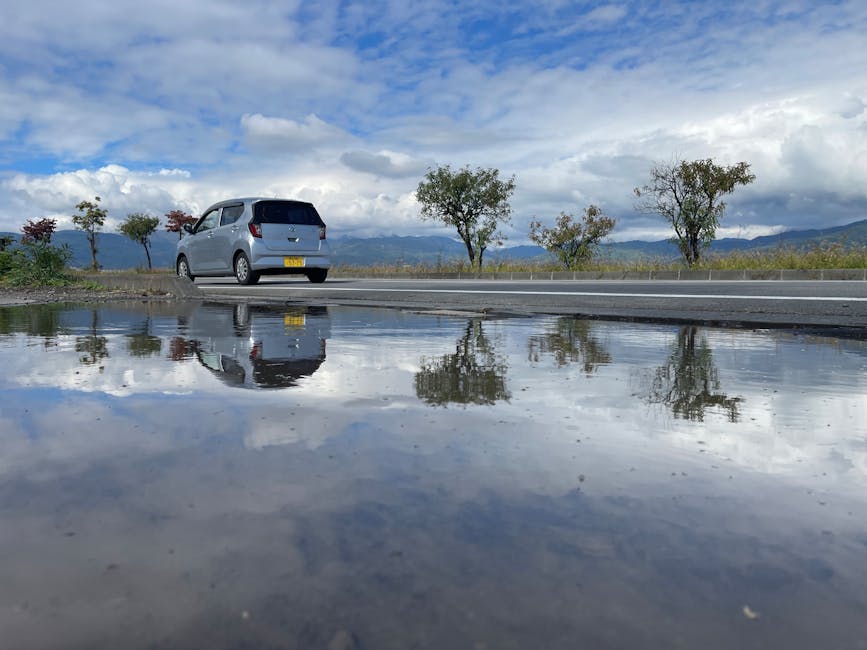道路を走る車が、美しい景色を背景に、道端の水たまりに美しく映っています。